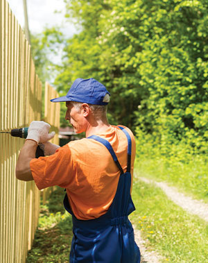 close-up-portrait-of-handy-carpenter-fixes-wooden-fence-with-cordless-electric-screwdriver